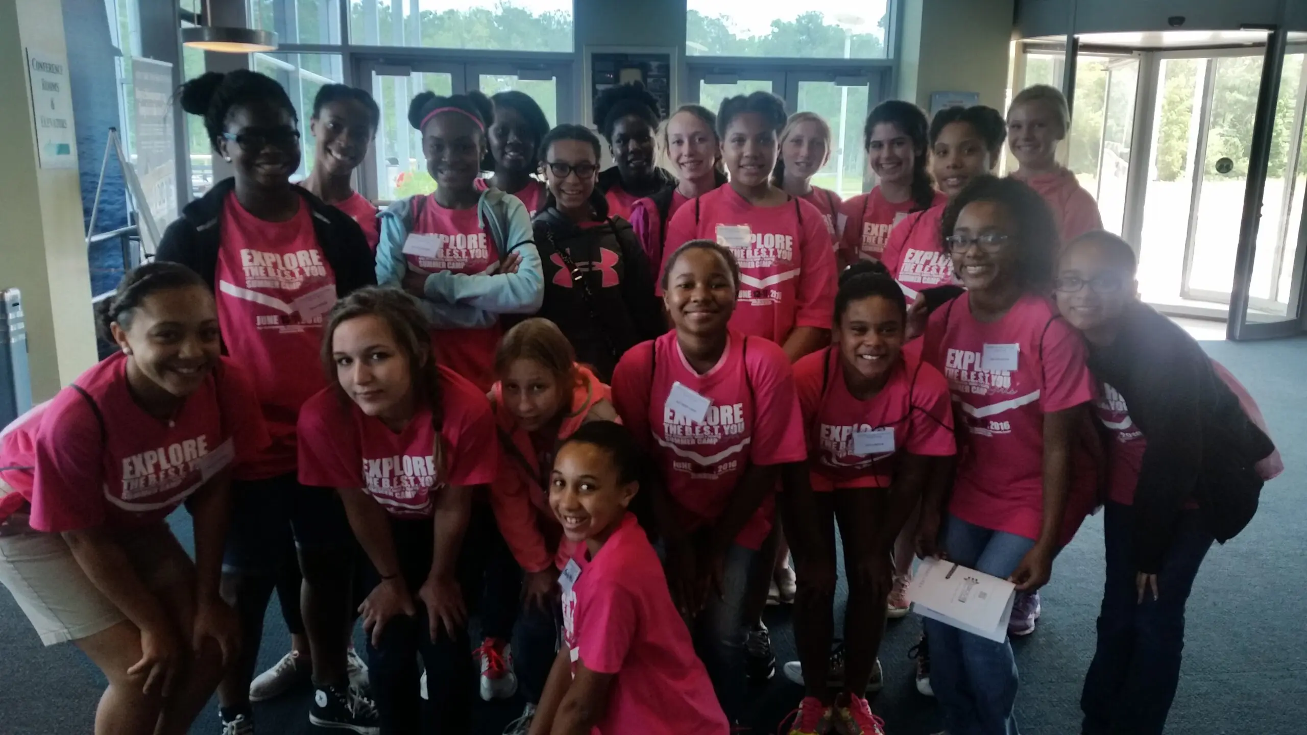 Diverse group of smiling young girls in pink 'Explore the B.E.S.T. You Summer Camp' t-shirts celebrating their summer learning journey.